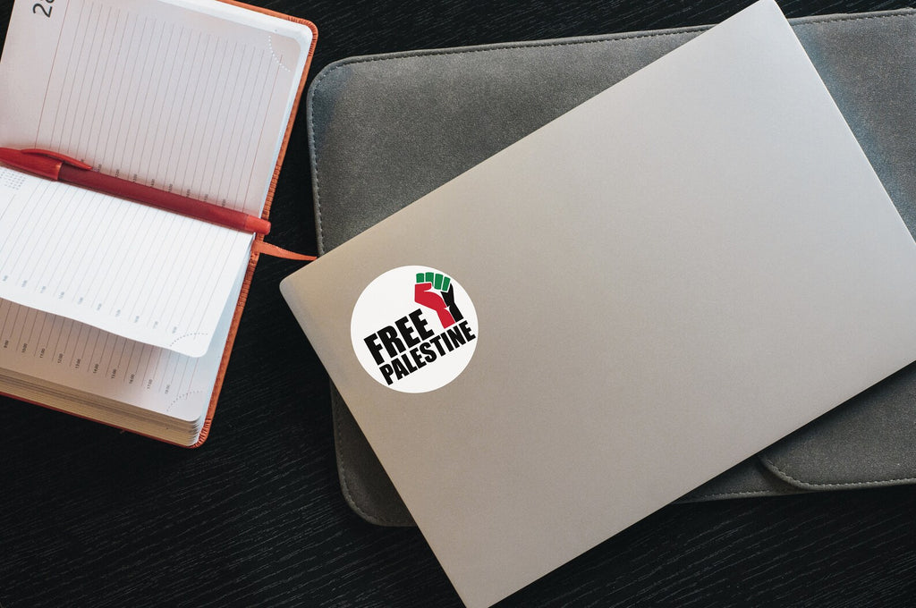 Free Palestine raised fist sticker on a closed silver laptop next to an open notebook