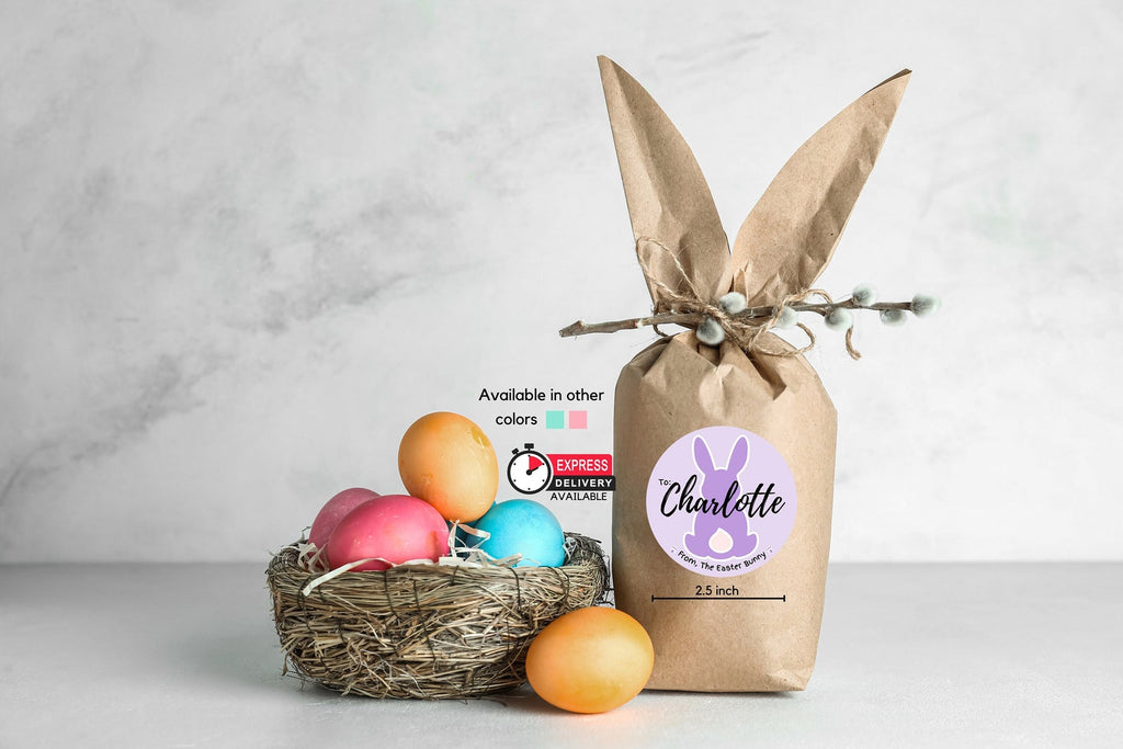 Purple Easter Bunny name sticker for Charlotte on a bunny-ear kraft treat bag beside a nest of Easter eggs