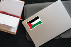 Stand With Palestine flag sticker on a closed silver laptop next to an open notebook and red pen